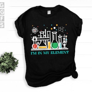 Könnte beinhalten: Schwarzes T-Shirt mit einer weißen Grafik von Bechergläsern und Reagenzgläsern. Der Text "I'm in my element" ist unter der Grafik gedruckt.