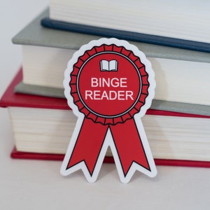 May include: A red and white sticker with a book icon and the text "Binge Reader" on a stack of four books. The books are gray, white, and red.