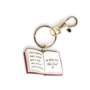 May include: Gold-tone book-shaped keychain with a red border. The keychain features the text "ONCE UPON A TIME, THERE WAS A GIRL WHO REALLY LOVED BOOKS... IT WAS ME. The End." with a heart symbol.
