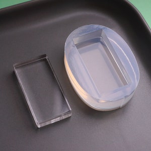 Peut inclure: Deux moules en silicone transparents pour la coulée de résine. Un moule est rectangulaire et l'autre est ovale avec un encastrement rectangulaire.