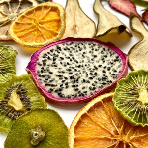 Puede incluir: Surtido de rodajas de fruta seca, incluyendo naranja, kiwi, fruta del dragón, pera y fresa. Las rodajas de fruta están dispuestas sobre una superficie blanca.