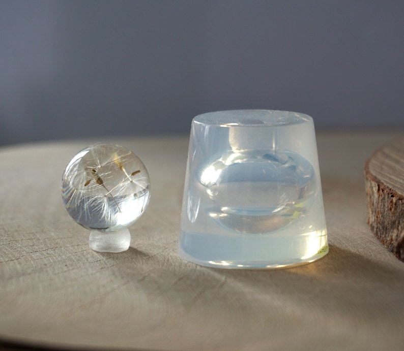 May include: Two clear silicone molds for resin casting. The smaller mold is a sphere and the larger mold is a cylinder. Both molds are empty.