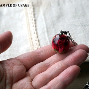 May include: A silver chain necklace with a round glass pendant containing a preserved red rose. The pendant is held in a hand.