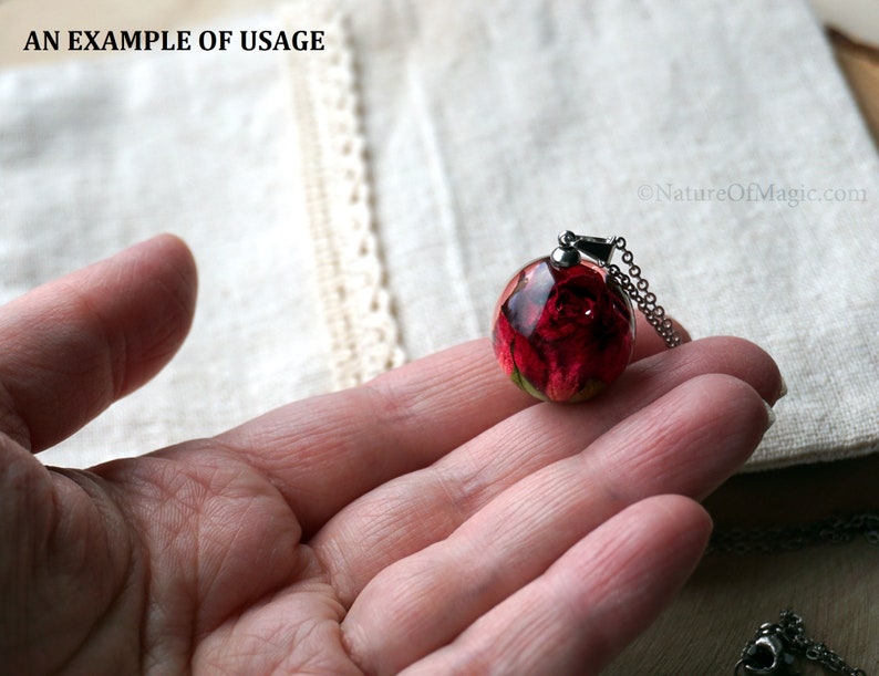 May include: A silver chain necklace with a round glass pendant containing a preserved red rose. The pendant is held in a hand.