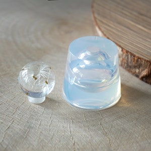 May include: Two clear resin molds, one round and one dome-shaped, for creating resin crafts. The round mold is smaller and has a flat base. The dome mold is larger and has a rounded base.