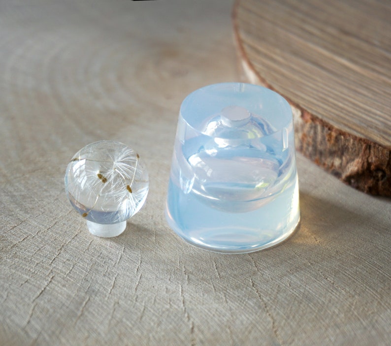 May include: Two clear resin molds, one round and one dome-shaped, for creating resin crafts. The round mold is smaller and has a flat base. The dome mold is larger and has a rounded base.