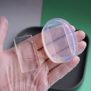 Peut inclure: Deux moules rectangulaires transparents, l'un en verre et l'autre en silicone, sont tenus dans une main gant&eacute;e. Le moule en silicone a une ouverture rectangulaire.