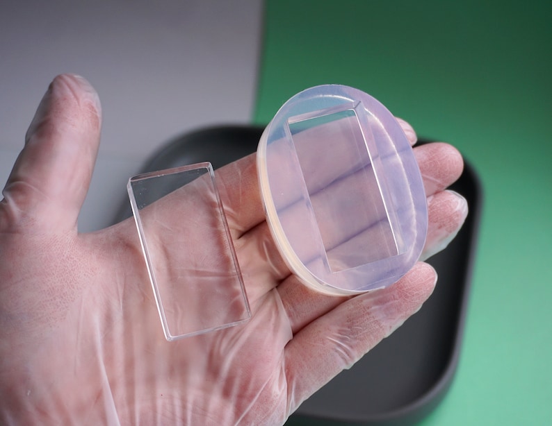 Peut inclure: Deux moules rectangulaires transparents, l'un en verre et l'autre en silicone, sont tenus dans une main gant&eacute;e. Le moule en silicone a une ouverture rectangulaire.