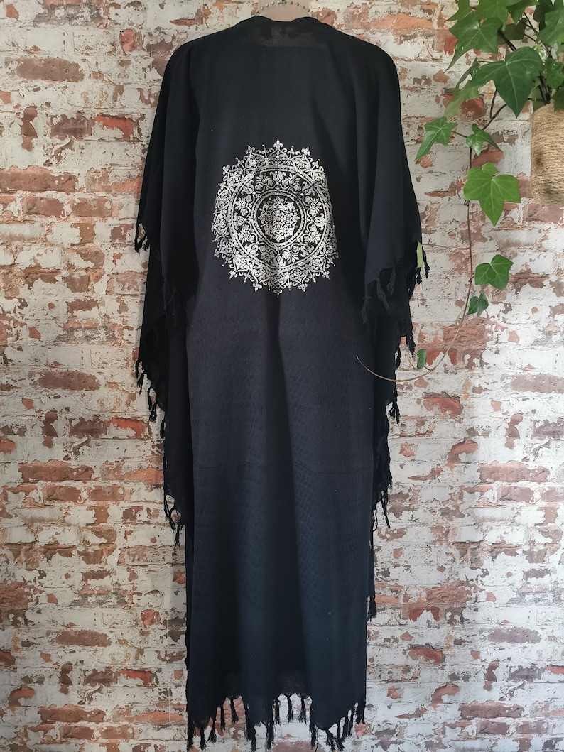 K&ouml;nnte beinhalten: Schwarzer Baumwoll-Kimono mit einem wei&szlig;en Mandala-Muster auf der R&uuml;ckseite. Der Kimono hat einen Fransenbesatz an Saum und &Auml;rmeln.