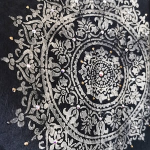K&ouml;nnte beinhalten: Ein silbernes Mandala-Design mit filigranen Details auf schwarzem Hintergrund. Das Mandala ist mit kleinen, klaren Strasssteinen verziert.
