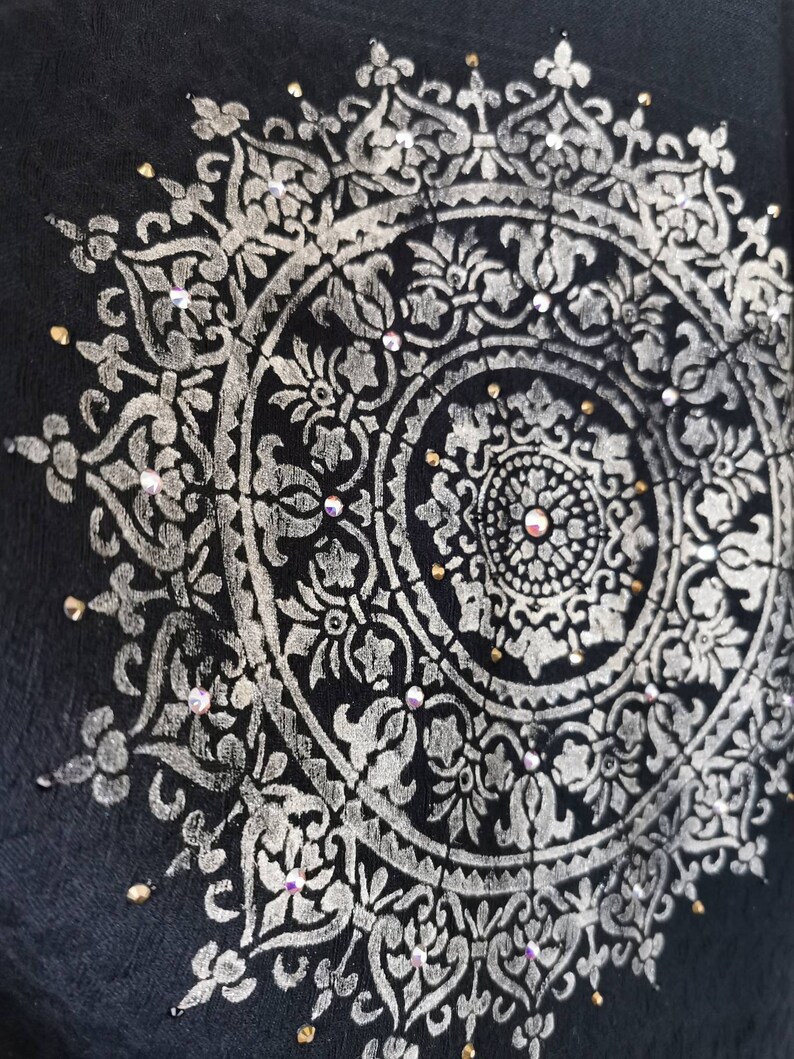 K&ouml;nnte beinhalten: Ein silbernes Mandala-Design mit filigranen Details auf schwarzem Hintergrund. Das Mandala ist mit kleinen, klaren Strasssteinen verziert.