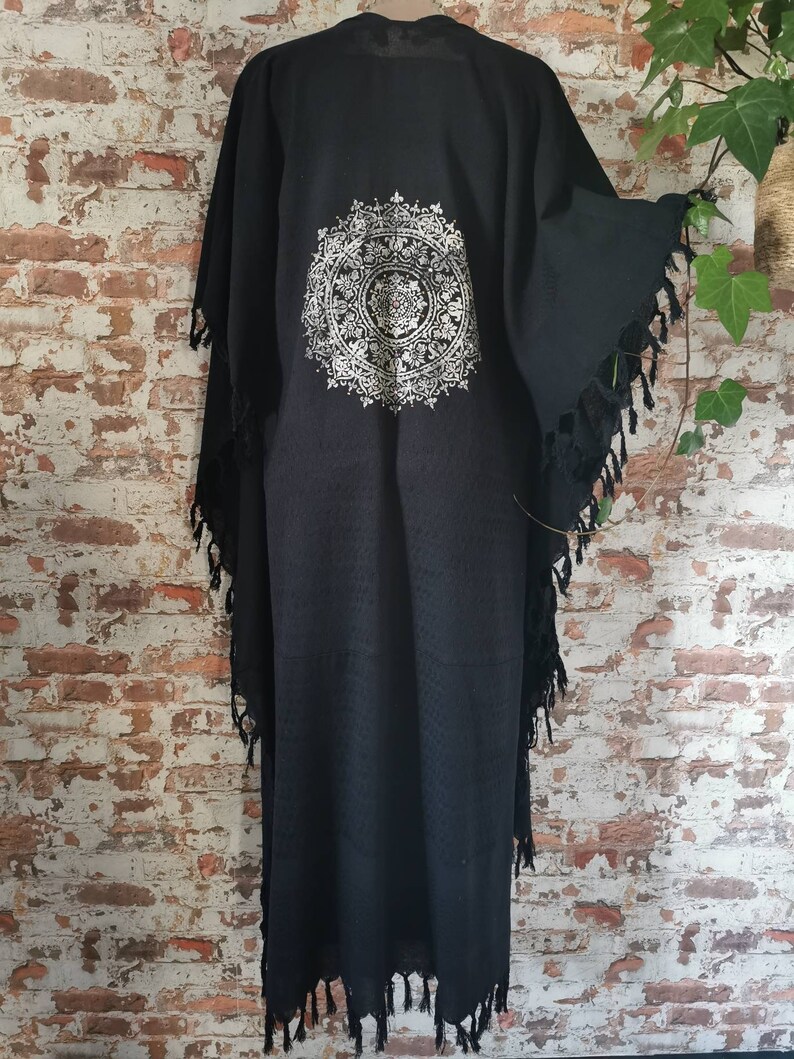 K&ouml;nnte beinhalten: Schwarzer Baumwoll-Kimono mit einem wei&szlig;en Mandala-Muster auf der R&uuml;ckseite. Der Kimono hat Fransen an den R&auml;ndern.