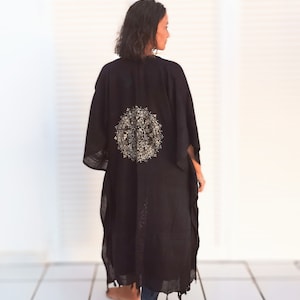 K&ouml;nnte beinhalten: Ein schwarzes Kimono mit einem goldenen Mandala-Muster auf dem R&uuml;cken. Das Kimono wird von einer Person getragen, die auf einem wei&szlig;en Fliesenboden steht.