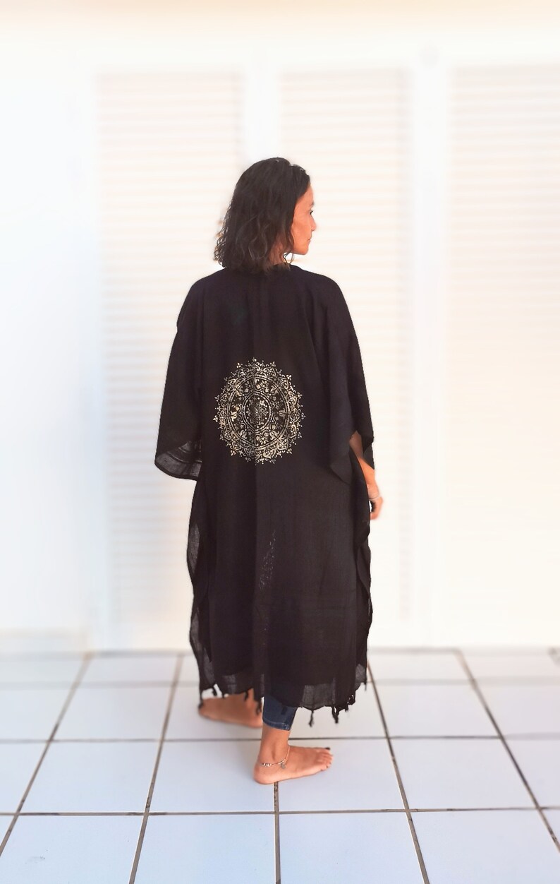K&ouml;nnte beinhalten: Ein schwarzes Kimono mit einem goldenen Mandala-Muster auf dem R&uuml;cken. Das Kimono wird von einer Person getragen, die auf einem wei&szlig;en Fliesenboden steht.