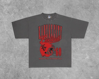 Puede incluir: Camiseta gris oscuro con las palabras "Kansas City Football" en rojo, un gráfico de casco de fútbol rojo y el número "60". El texto "Kansas City, Missouri 1960" está impreso debajo del casco.