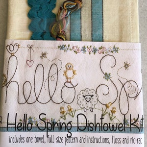 May include: A Hello Spring Dishtowel Kit includes a cream-coloured dishtowel with blue stripes, embroidery floss, a teal-coloured ric-rac trim, and a pattern with instructions. The embroidery pattern features a stitched design of a chick, a sheep, and the words "Hello Spring".