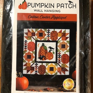 Puede incluir: Un patrón para una pared colgante de parche de calabaza con una aplicación central de algodón. El patrón presenta un diseño de patchwork con calabazas, cuervos y una luna creciente. El patrón es de Shabby Fabrics.