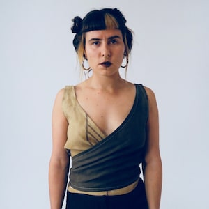 May include: A woman wearing a brown and beige wrap top with a deep V-neckline. The top is sleeveless and has a criss-cross design in the front.
