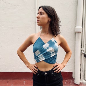 Könnte beinhalten: Ein blaues und weißes Batik-Halter-Top mit einem Kreuzdesign. Das Top wird mit einem schwarzen Jeansrock getragen.