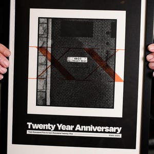 May include: Framed art print with the text "AN EMERGENCY SCENE" at the top. The print features a black and white design with orange accents and the text "Twenty Year Anniversary". The bottom text reads "WE WENT THROUGH THE SAME DOOR. WE ENDED UP IN SO MANY DIFFERENT PLACES."