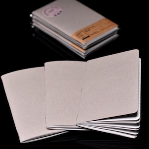 May include: Three gray notebooks with lined pages are open and fanned out on a black surface. The notebooks have a textured paper cover.