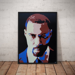 May include: A framed portrait with a black border. The artwork features a stylized depiction of a person's face, rendered in shades of red, blue, black, and white against a black background. The portrait is displayed on a wooden floor.