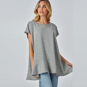 May include: A grey, short-sleeved tunic top with a rounded neckline and a flared hem. The top is made of a soft fabric and is a solid colour. The model is wearing blue jeans. This top is suitable for casual wear.