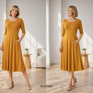 Op de afbeelding: Mosterdkleurige midi-jurk met een ronde hals en driekwart mouwen. De jurk heeft zakken en een uitlopende rok. Het woord "MUSTARD" staat onderaan de afbeelding.