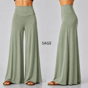 Puede incluir: Pantalones de pernera ancha y cintura alta en color verde salvia, mostrados de frente y de lado. Los pantalones presentan un color s&oacute;lido, una textura de tela suave y una silueta ancha y fluida que llega hasta el suelo. El texto SAGE est&aacute; impreso en el centro.