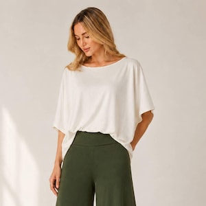 Op de afbeelding: Een losvallende, crèmekleurige top met korte mouwen en een brede boothals, gecombineerd met een olijfgroene broek met hoge taille en wijde pijpen. De top heeft een ontspannen pasvorm en de broek heeft een gladde, effen afwerking.