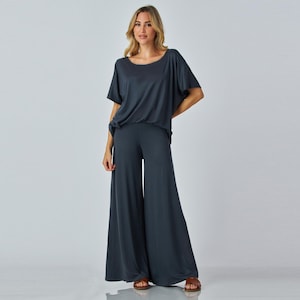 Puede incluir: Conjunto de dos piezas gris oscuro con pantalones palazzo y un top a juego de manga corta. El top tiene cuello redondo y corte holgado. Los pantalones de pernera ancha son largos hasta el suelo. El conjunto es de tejido suave y fluido.