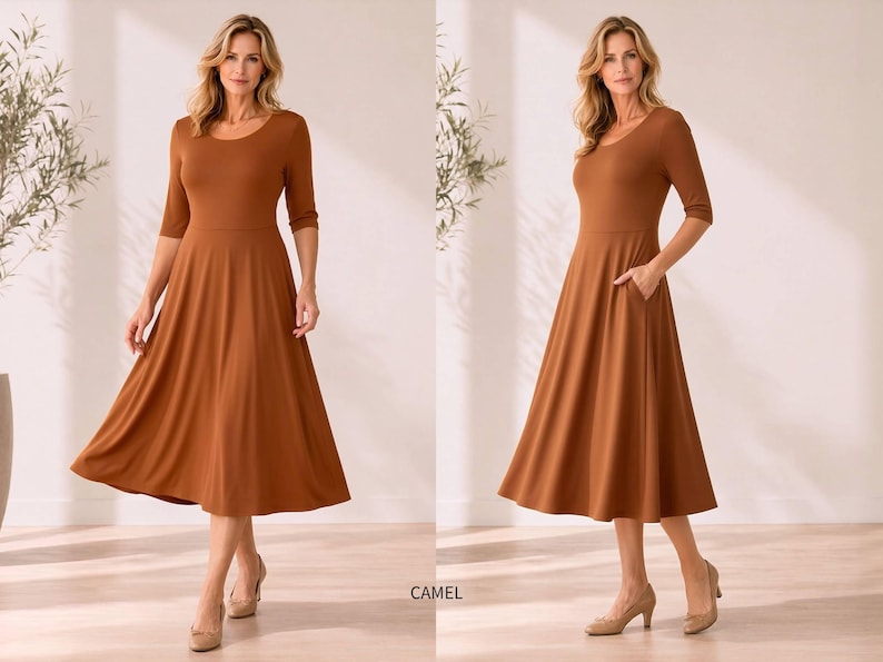 Op de afbeelding: Een camelkleurige jurk met een ronde hals en driekwartmouwen. De jurk heeft een getailleerd lijfje en een uitlopende rok die tot halverwege de kuit valt. De jurk heeft zakken. Het model draagt beige hakken.