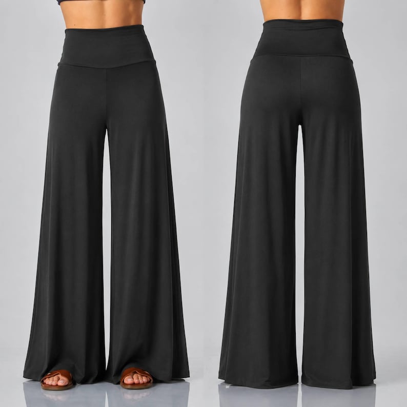 Puede incluir: Un par de pantalones negros lisos de talle alto y pernera ancha, mostrados desde la parte delantera y trasera. Los pantalones cuentan con una cintura lisa y ajustada sobre las caderas y caen en perneras sueltas hasta el suelo con dobladillo.