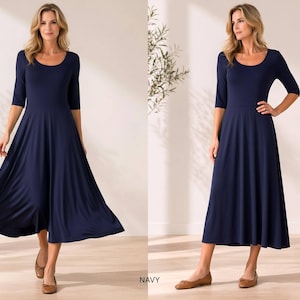 Op de afbeelding: Marineblauwe midi-jurk met een ronde hals en driekwartmouwen. De jurk heeft een getailleerd lijfje en een uitlopende rok. Het model draagt bruine ballerina's. Het woord "NAVY" staat onderaan de afbeelding.