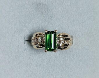 Può includere: Un anello d'oro con uno smeraldo verde e piccoli diamanti incastonati nella fascia.