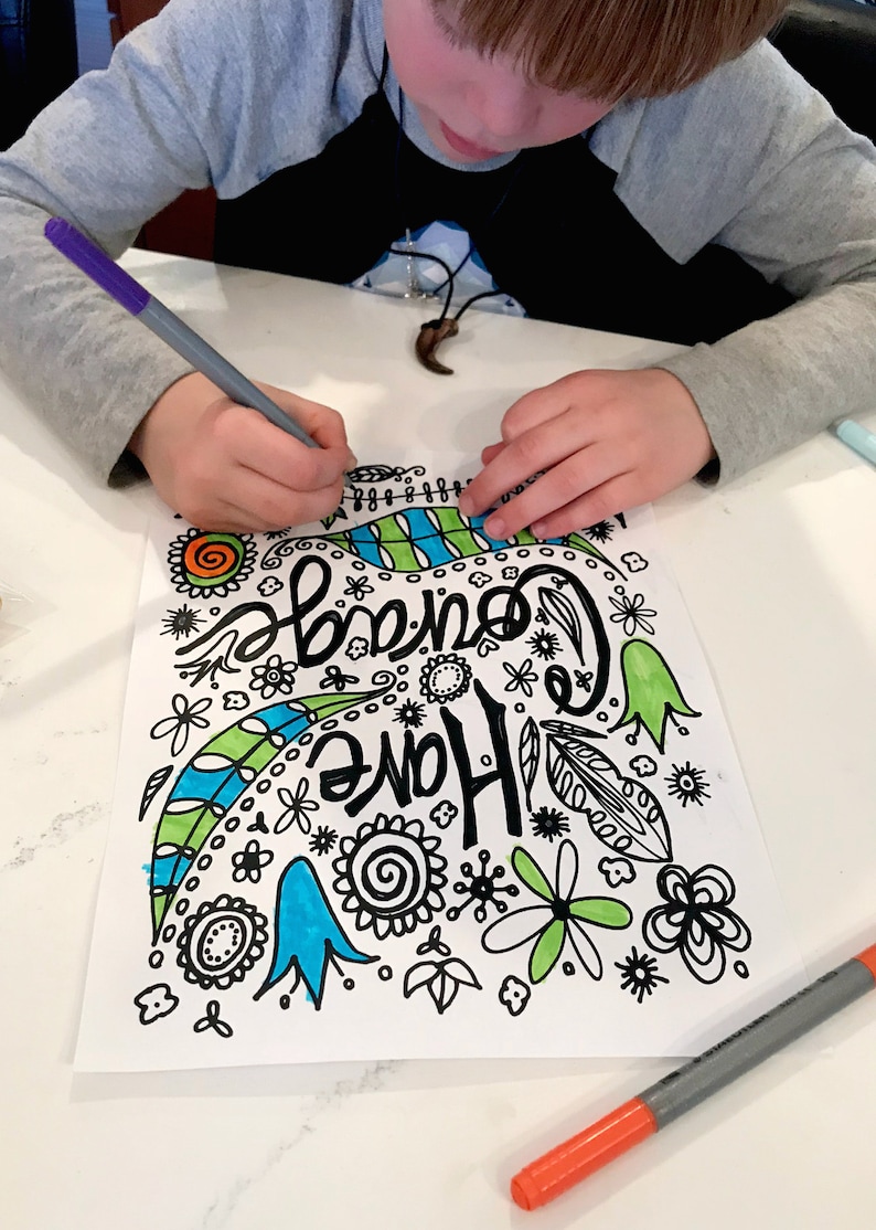May include: A child colors a black and white drawing of a colorful design with the words "Come Home" in a whimsical font. The drawing includes flowers, leaves, and swirls. The child is using a purple marker to color the drawing.