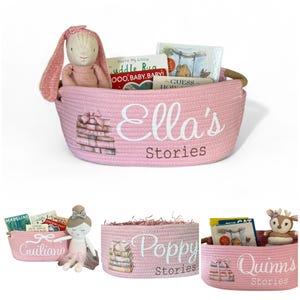 Peut inclure: Panier de rangement rose tiss&eacute; avec le texte "Ella's Stories" et un graphisme de pile de livres. Le panier contient un lapin en peluche, des livres et d'autres jouets. D'autres paniers avec des noms diff&eacute;rents sont &eacute;galement pr&eacute;sent&eacute;s.