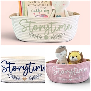 Puede incluir: Una cesta de cuerda blanca con la palabra "Storytime" bordada en escritura verde, junto con motivos de hojas y corazones. La cesta contiene libros y una mu&ntilde;eca de peluche. Se muestran cestas adicionales en rosa y blanco.