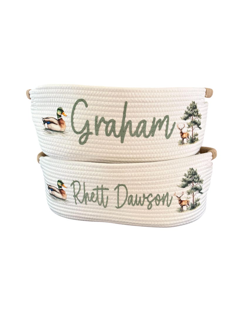 Peut inclure: Deux paniers en corde blanche avec des poign&eacute;es marron. Chaque panier porte un nom en &eacute;criture verte, ainsi qu'un canard et un cerf. Un panier dit "Graham" et l'autre "Rhett Dawson".