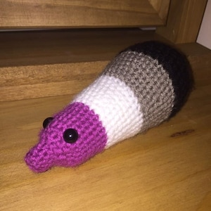 May include: A crocheted plush toy shaped like a worm with a purple, white, gray, and black striped body. The toy has two black eyes.