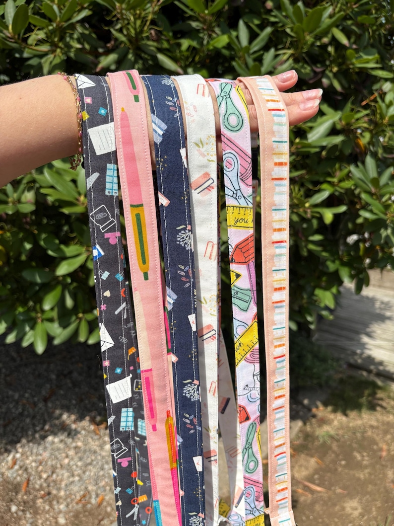 K&ouml;nnte beinhalten: Eine Sammlung von sechs Stoffb&auml;ndern mit verschiedenen Mustern von Schul- und B&uuml;robedarf. Die Designs zeigen Illustrationen von Stiften, Scheren, Linealen, B&uuml;roklammern und Umschl&auml;gen in Farben wie Schwarz, Pink, Marineblau, Wei&szlig; und Gelb.