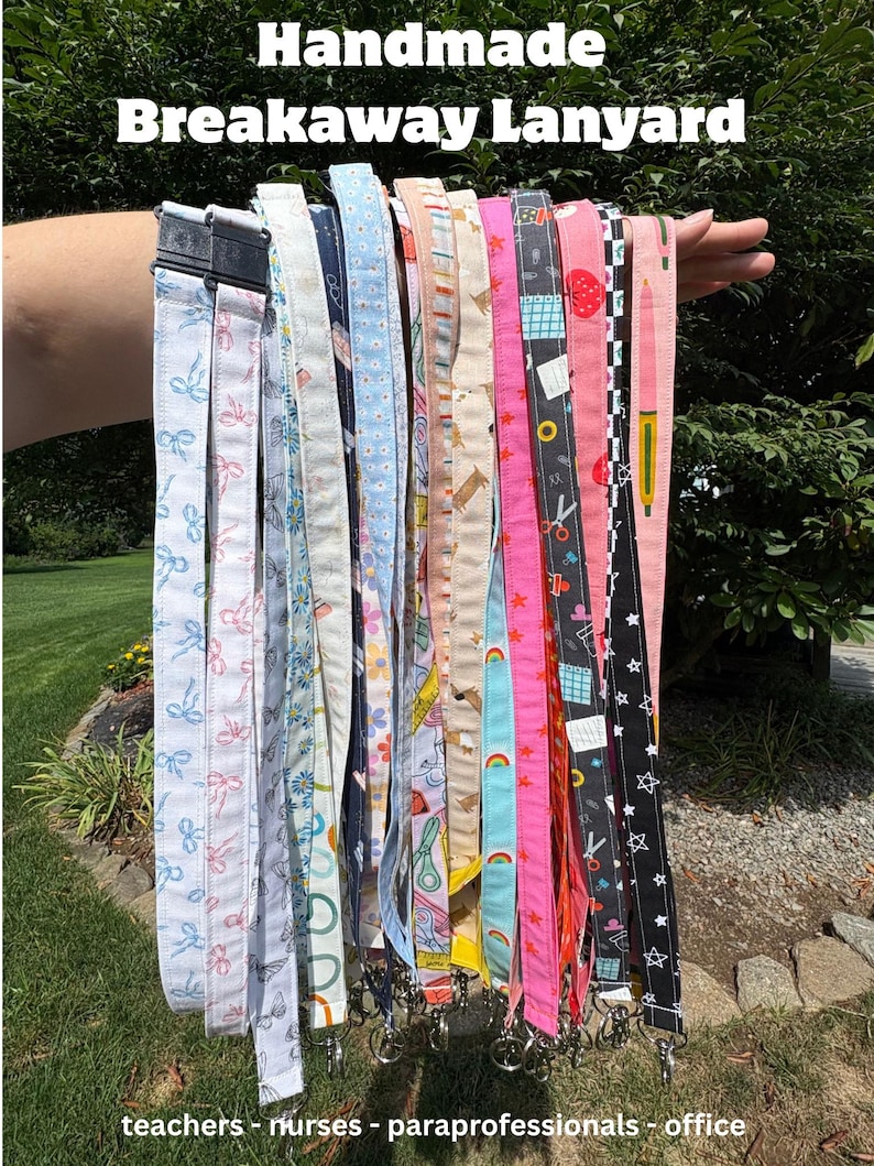 K&ouml;nnte beinhalten: Eine Sammlung von Stoff-Lanyards mit Sicherheitsverschluss, die verschiedene Muster wie Schleifen, Blumen, Regenb&ouml;gen, Sterne und Schulbedarf zeigen, jeweils mit einem schwarzen Kunststoff-Sicherheitsverschluss und einem Metallhaken.