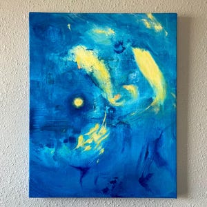 May include: Abstract painting on canvas with a deep blue background and yellow brushstrokes. The artwork features a circular yellow shape and dynamic, flowing forms, creating a sense of movement and depth. The painting is mounted on a wooden frame.