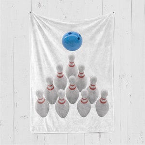 May include: A white fleece blanket with a blue bowling ball and ten white bowling pins arranged in a triangle shape.