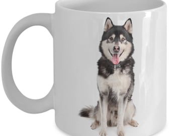 May include: White ceramic coffee mug with a black and white Alaskan Malamute dog sitting on a white background.