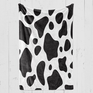 May include: A white and black cow print fleece throw blanket. The blanket has a soft, plush texture and is perfect for snuggling up on the couch.