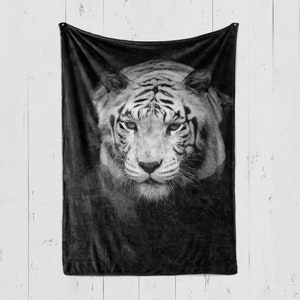 Puede incluir: Un tigre blanco con ojos azules mira directamente a la c&aacute;mara. El tigre est&aacute; enfocado, mientras que el fondo est&aacute; desenfocado y oscuro.