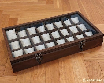 Op de afbeelding: Een donkerbruine houten horlogebox met een glazen deksel en 20 individuele vakken die zijn gevoerd met zacht stof. De doos heeft een metalen sluiting en is ideaal voor het opbergen en tentoonstellen van horloges.