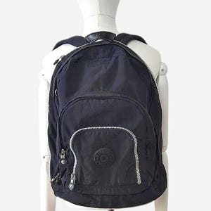 May include: Black backpack with a rounded shape, featuring a front pocket and silver zippers. The backpack has a circular logo patch on the front and a top handle. The bag is displayed on a white mannequin.