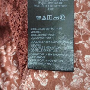 May include: A close-up of a clothing label with text in English and French. The label details fabric content, such as cotton, viscose, and nylon. The background features a floral pattern in brown and white.